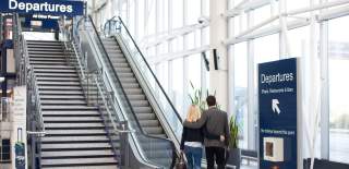 2 people stepping on a escelator going up to the departure lounge at Bristol Airport - Credit Bristol Airport
