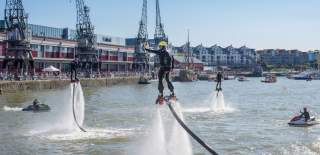 A man wearing a water-powered jetpack performing stunts on Bristol's Harbourside during the Bristol Harbour Festival with the M Shed local history museum in the background - credit Jim Cossey