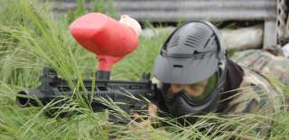 A person lying in tall grass aiming a paintball gun at Bristol Activity Centre - credit Bristol Activity Centre