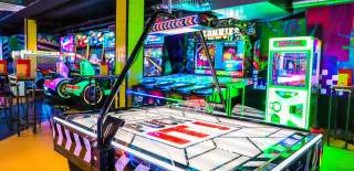 Brightly lit bar interior with arcade machines and air hockey table - credit King Pins