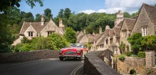 A red vintage sports car driving over the bridge in the village of Castle Combe, near Bristol - credit Great West Way