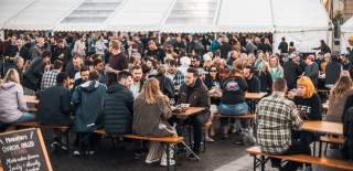 People sat on wooden benches outside drinking beer - Credit Craft Beer Festival