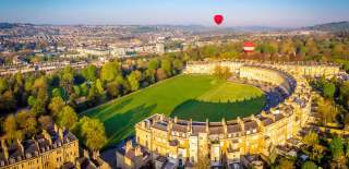 An aerial view of the Royal Crescent in Bath near Bristol, with hot air balloons launching from the green
