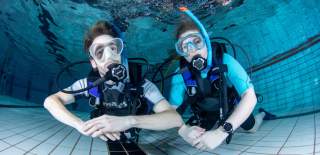A man and woman posing underwater in an open water diving course with PADI Bristol - credit PADI