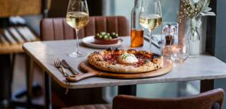 A pizza on a table with two glasses of wine at Pizza on the Park in central Bristol - credit Evoke Pictures