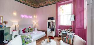 A lounge area with large window, pink wall and white furniture - credit Mint Stays