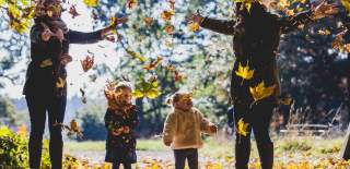 Two mothers and their young daughters throwing fallen leaves in the grounds of Westonbirt Arboretum near Bristol in autumn - credit Johnny Hathaway