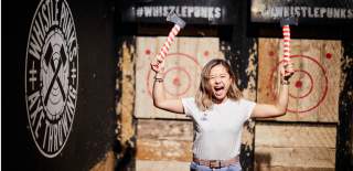 A woman cheering while holding two axes at the Whistle Punks Bristol Axe Throwing experience - credit Whistle Punks