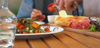 A diner enjoys a bright plate of food, including a salad and a charcuterie board.