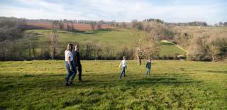Two boys walk ahead of their parents across a field near Blockley, with trees and hills in the distance.