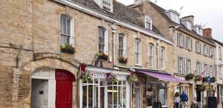A couple walking past shops with pretty frontages and hanging baskets in Chipping Norton town centre