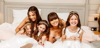 Bridesmaids hug and smile on a bed before a wedding ceremony