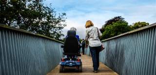 Lady crossing bridge in wheelchair with carer at Westonbirt Arboretum