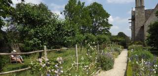 Two people sitting on a bench in the garden at Kelmscott Manor. A fence made of fallen wood from trees on the estate lines the gravel pathway.