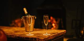 Two glasses of champagne and bottle on a table in front of an open fire