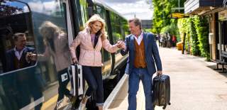 A couple disembark a train carrying suitcases at Kingham station