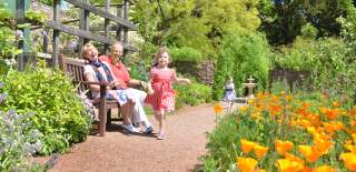 little girl running through an alley in a garden whilst grandparents are watching on from a near bench