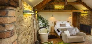 photo of converted barn with a bed and bathtub @ the Yard Devon Yurts