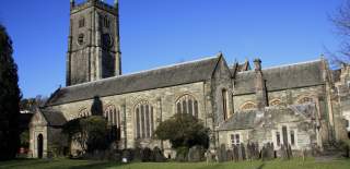 A historic stone church with a tall clock tower stands against a clear blue sky. The scene conveys a serene and timeless atmosphere.