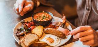 A close up of a person holding a knife and fork as they're about to start eating a cooked breakfast.