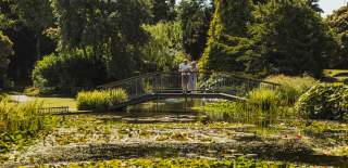 A couple stood on the bridge at Burnby Hall Gardens surrounded by lush greenery