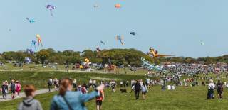 A large crowd walking towards the Bridlington Kite Festival, with kites floating in the air in the distance