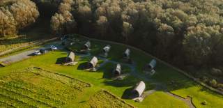 An aerial view above Flamborough Glamping and Vineyard. Eight glamping pods look out onto a newly established vineyard and are backed by lots of mature trees.