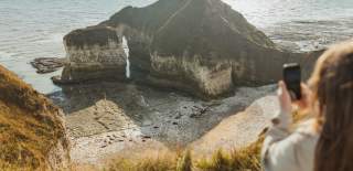 A woman taking a photo of the drinking dinosaur at Flamborough Head on mobile phone.