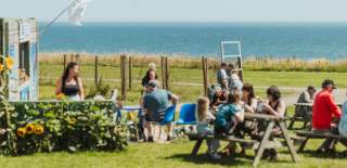 A group of people sat outside in the sunshine enjoying refreshments from Blu Savannah in Bridlington. The sea is visible in the background.