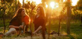 Two people enjoying a glass of wine amongst the vines at golden hour at Laurel Vines Vineyard and Winery.