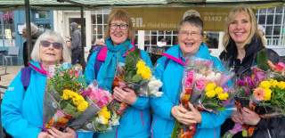 Three HEY volunteers in their iconic blue uniforms giving out flowers in Beverley's Saturday Market, along with a member of staff from HEY Volunteering.