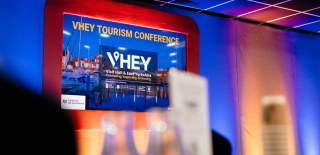 A screen on stage at the VHEY tourism conference 2024 displaying the VHEY logo.