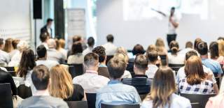 Delegates listening attentively as a man speaks on stage at a business conference.