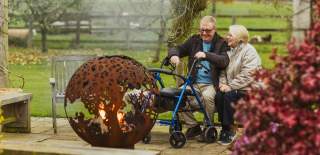 A couple sat around a fire pit in the gardens of Broadgate Farm Cottages in East Yorkshire. The male has a rollator by his side.