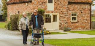A couple walking the grounds at Broadgate Farm Cottages in East Yorkshire. The man is walking with the aid of a rollator.