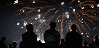 A crowd of people watch fireworks exploding overhead at a display.