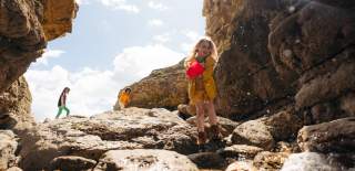 A little girl surrounded by the rocks at Thornwick Bay with her family in the background