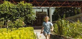 Little boy running through Hull Museums Quarter gardens  towards the camera wearing noise cancelling headphones