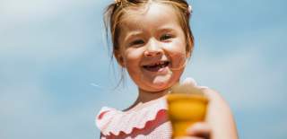 Little girl smiling in the sunshine, holding an ice cream on a beach in East Yorkshire