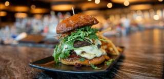Gourmet burger with juicy beef, cheese, arugula, and crispy onions on a toasted bun, served with fries in a Gwinnett restaurant.