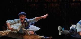 Performer in vintage attire leaps with newspapers on Aurora Theatre’s dynamic stage.