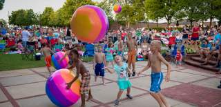 Children playing with colorful beach balls at a lively outdoor event at Duluth Beach, with a large audience enjoying the summer atmosphere.