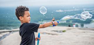 A child blows bubbles on a rocky overlook at Stone Mountain Park, capturing a joyful moment of play and nature.
