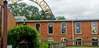 The brick building of Tannery Row Artist Colony with a large art sign, is surrounded by lush green plants in Buford, Georgia.