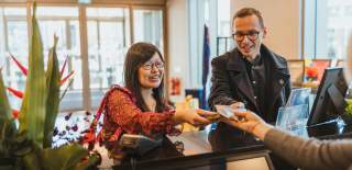 A smiling woman and man stand at the hotel reception desk of the DoubleTree by Hilton, Hull handing documents to a receptionist whose arm is extended towards them.
