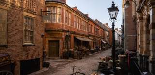 Hullywood film set recreating a historic cobbled street lined with brick buildings, vintage shopfronts, market stalls, wooden barrels and old‑style street lamps, capturing an authentic period atmosphere.