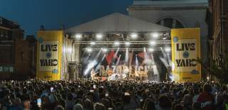 A crowd show of a stage at night with a yellow surround stating Live at the Yard.