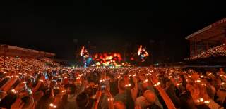 A crowd shot of Coldplay performing at Craven Park, the crowd are wearing wristbands with orange lights.