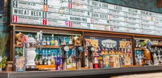 The interior of Taphouse on Humber Street in Hull, a wide assortment of colourful bottles sit behind a bar. Above sits a sign with a large variety of different drinks on offer.