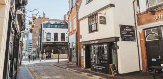 Cobbled street in Hull’s Old Town featuring historic brick buildings, traditional pubs and people walking in the sunshine
